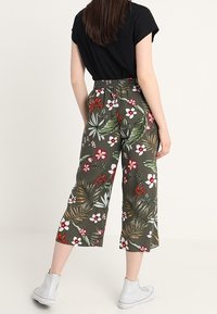 Green floral patterned culottes with a high waistband, elastic back, featuring white and red blossoms, paired with white sneakers.