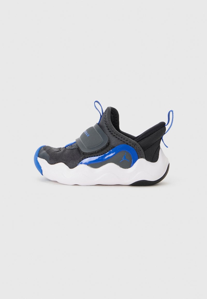 Baskets sportives noires et bleues pour tout-petit, avec semelle blanche ondulée, bride velcro et languettes sur la languette et le talon sur fond uni.