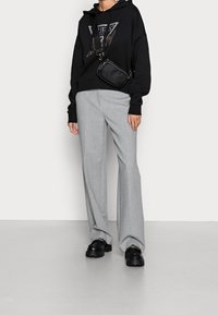 Black hooded sweatshirt with a logo, light gray wide-leg pants, and black chunky shoes, paired with a small black crossbody bag.