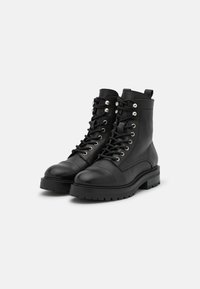 Bottines noires en cuir avec un laçage à l'avant, bouts ronds, œillets métalliques et une semelle épaisse et texturée. Construction robuste avec une languette.