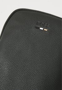 Pouch in pelle nera testurizzata, caratterizzato dal logo "BOSS" in rilievo con dettagli in nero, bianco e oro. Chiusura con zip lungo il bordo superiore.