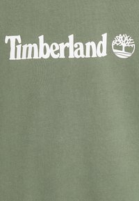 Felpa verde oliva con logo bianco "Timberland" e emblema dell'albero. Realizzata in tessuto morbido con texture liscia.