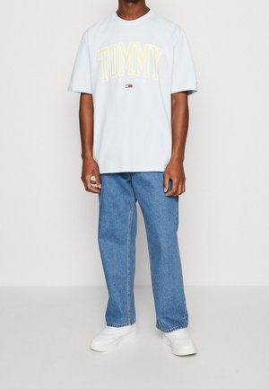 Lichtblauw katoenen T-shirt met "TOMMY JEANS" in geel gedrukt. Gecombineerd met losse blauwe spijkerbroeken en witte sneakers. Eenvoudig ontwerp, relaxte pasvorm.