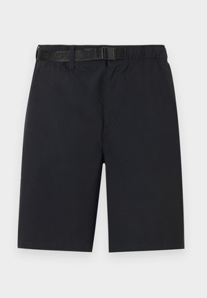 Άνδρας που φοράει μαύρα cargo σορτς μήκους μέχρι το γόνατο με ζώνη, λευκές κάλτσες και λευκά αθλητικά Nike με μαύρα λογότυπα Swoosh.