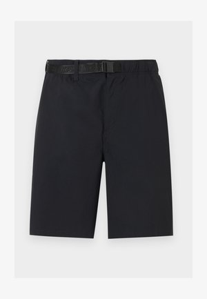 Hombre con pantalones cortos cargo negros hasta la rodilla con cinturón, calcetines blancos y zapatillas blancas Nike con logos negros de Swoosh.