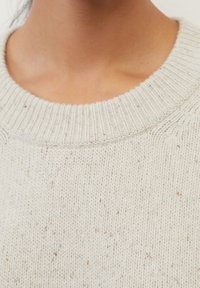 Harmaa neulepaita, jossa on ribbireunus ja pyöreä kaula-aukko, pehmeällä tekstuurilla ja pienillä tummemmilla täplillä kankaan sisällä.