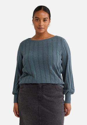 Blauer, gerippter Strickpullover mit lockerer Passform, weitem Ausschnitt und voluminösen Ärmeln, kombiniert mit einem grauen Jeansrock.
