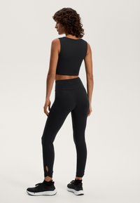 Črn športni crop top in leggingi z visokim pasom iz gladkega materiala. Leggingi imajo izrezane detajle na robu. Dopolnjeni z črnimi športnimi copati.