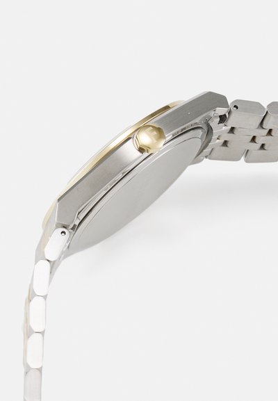 Silver stainless steel watch with a gold-tone accent on the bezel, featuring a rounded case, hexagonal link bracelet, and crown detail.