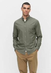 Olijfgroene blouse met knopen, een kraag, een borstzak en lange mouwen, gecombineerd met beige broek. Gelaagd stof met een gladde afwerking.