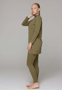 Olijfgroene lange mouw tuniek met hoge kraag, gecombineerd met passende leggings, gemaakt van glad, rekbaar materiaal, aangesloten silhouet.