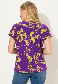 Paarse t-shirt met een geel vogelpatern, korte mouwen en een ontspannen pasvorm. De stof lijkt zacht met een gladde textuur.