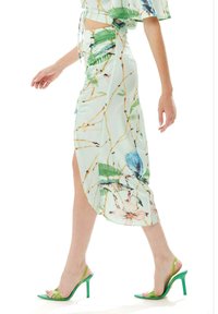 Light blue midi skirt with tropical bird and leaf print, featuring a high slit, buttons, and paired with green strappy heeled sandals.