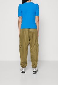 Blå puffärmad topp i kombination med olivgröna cargobyxor som har sidofickor och elastiska ärmslut. Bärs med silvriga sneakers.