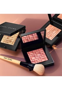 Compact make-up paletten in glanzend zwarte verpakkingen bevatten textuurblush en highlighter tinten. Een zachte borstel heeft een houten handvat.