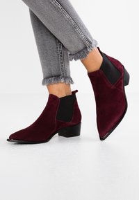 Burgundy suede ankle boots with a pointed toe, elastic side panels, and a low block heel, paired with frayed grey jeans.