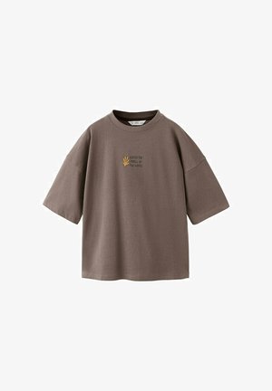 T-shirt marron ample à manches courtes avec un col rond et un petit motif jaune de main accompagné du texte "Attrapez le frisson des vagues" sur la poitrine.