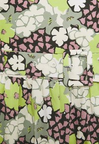 Květinová látka s bílými, zelenými a růžovými květy, která obsahuje odpovídající pásek s obdélníkovou sponou a průvleky na nařaseném materiálu.