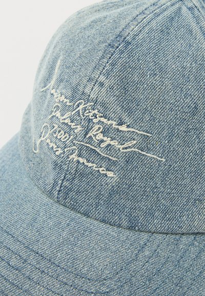 Ανοιχτό μπλε τζιν καπέλο μπέιζμπολ με λευκό κείμενο σε καλλιγραφική γραφή κεντημένο στο μπροστινό πάνελ, με ορατή ραφή στη καμπυλωτή γείσο και τις ραφές.
