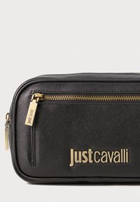 Juodas tekstūruotas užtrauktukas su auksine aparatūra ir ženklinimu "Justcavalli", su išsiskiriančiu užtrauktuku viršuje, kad būtų lengva pasiekti.