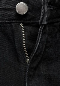 Černé jeansy z denimu s kovovým knoflíkem, stříbrným zipem a texturovaným povrchem, které zvýrazňují oblast předního zipu.