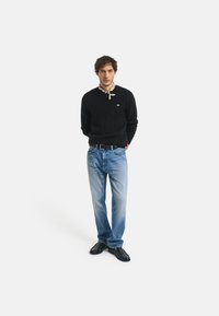 Pulover negru din tricot cu model, blugi din denim bleu deschis, pantofi negri, cu o bentiță cu model. O ținută simplă și casual, cu un design clasic.