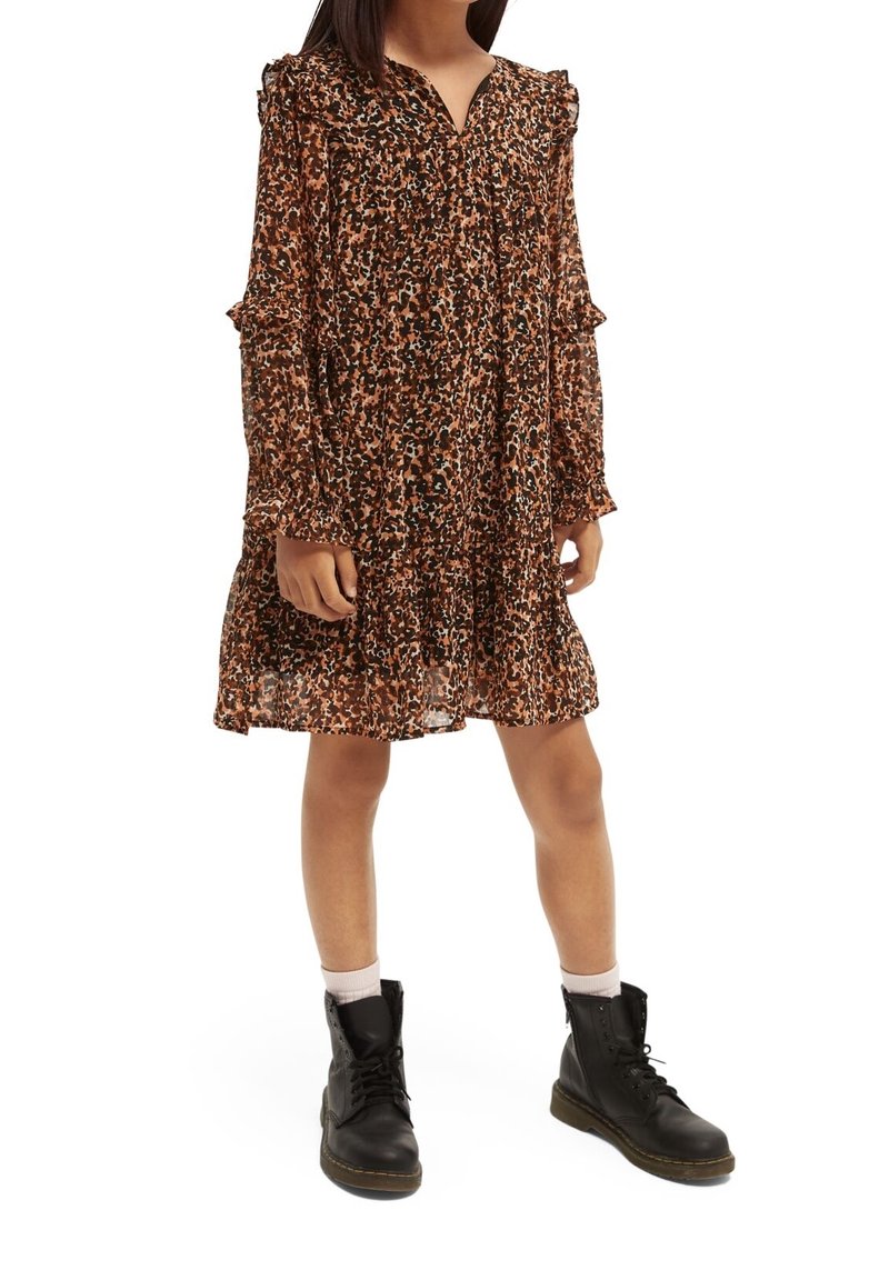 Jeune fille portant une robe longue à manches longues florale marron et noire, associée à des bottines noires à lacets et des chaussettes de couleur claire.