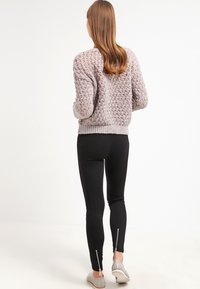 Neule vaaleanharmaa villapaita, jossa on löysä istuvuus ja teksturoitu kuosi, yhdistettynä mustiin legginsseihin, joissa on nilkkavetoketjut ja harmaat liukuesteet.