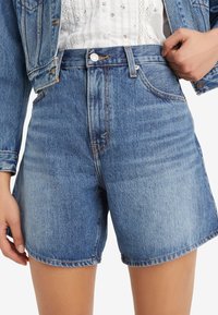 Světle modré džínové kraťasy s vysokým pasem a rovný střihem. Mají přední kapsy, zapínání na knoflík a viditelné švy.