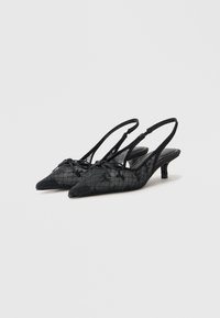 Chaussures noires à talon fermé et à bout pointu avec une superposition de dentelle texturée, présentant un motif à carreaux subtil.