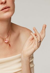 Collares en capas de oro y rosa con un colgante en forma de estrella y detalle geométrico. Anillo sencillo de plata llevado en la mano con acabado de uñas naturales.