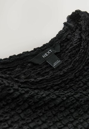 Schwarzes, strukturiertes Oberteil mit einem zerknitterten Muster, Rundhalsausschnitt und einem Etikett mit dem Markennamen "NEXT". Weicher, leichter Stoff.