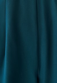 Teal fabric with a smooth texture, featuring folds that create a fluid appearance, suitable for clothing or drapery.