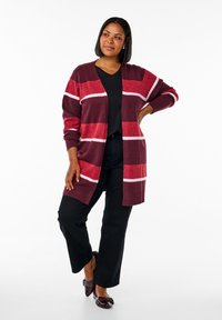 Lång mörk röd cardigan med vita och rosa horisontella ränder. Tillverkad av mjukt material, med ribbade manschetter och en öppen framsidesdesign.