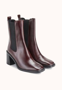 Paire de bottines en cuir marron foncé avec talons carrés et panneaux latéraux élastiques noirs sur fond blanc.