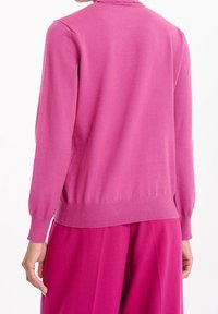 Figursydd rosa tröja med ribbstickade muddar och fåll, slät textur och hög halsringning. Sydde detaljer längs kragen.