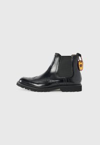 Bottines Chelsea en cuir noir avec un bout arrondi, des panneaux élastiques sur les côtés, des détails de brogue décoratifs, une semelle en caoutchouc et une languette à l'arrière.