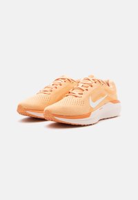 Sapatilhas de corrida Nike com um cabedal em malha laranja claro e detalhes brancos. Apresentam biqueira arredondada, sola texturizada e um design respirável.