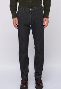 Ciemnoszare dżinsy o wąskim kroju, z zapięciem na guzik z przodu i pięcioma kieszeniami, w zestawieniu z brązowymi butami wizytowymi.