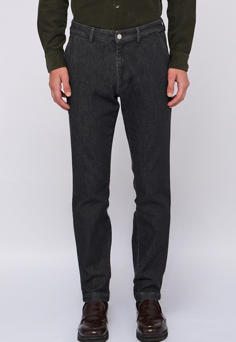 Ciemnoszare dżinsy o wąskim kroju, z zapięciem na guzik z przodu i pięcioma kieszeniami, w zestawieniu z brązowymi butami wizytowymi.