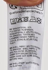Fabric care label with text in multiple languages, predominantly white background, detailing materials: 93% polyester, 7% spandex; care instructions included.
