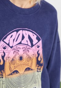 Navyblaues Sweatshirt mit einem großen, bunten Grafikdesign von Palmen, Sonne und Wellenmustern; weiche Textur und lässige Passform.