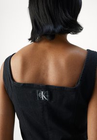 Svart denimkjole med firkantet utringning, brede stropper og et Calvin Klein Jeans-merke på baksiden. Glatt tekstur og skreddersydd passform.