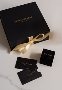 Zwarte cadeau doos met gouden letters, vastgebonden met een gele satin lint. Bevat een zwarte fluwelen ringdoos en twee zwart kaartjes met gouden accenten.