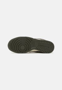 Shoe sole med en tekstureret mørkegrøn gummioverflade, der har et cirkulært mønster, riller og et fremtrædende logo nær hælen.