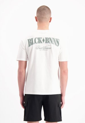 Witte katoenen t-shirt met groene grafische tekst op de achterkant, korte mouwen en een losse pasvorm, gecombineerd met zwarte cargoshorts.