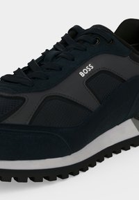 Chaussure de sport noire et gris foncé avec lacets noirs, semelle texturée et logo "BOSS" sur la partie latérale.