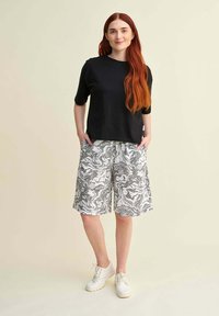 Mustat lyhyet hihalet paidat, joissa on pyöreä pääntie, yhdistetty polvimittaisiin shortsseihin, joissa on mustavalkoinen abstrakti kuvio. Valkoiset lenkkarit viimeistelevät asun.