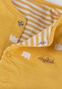 Gelbes Kinderhemd mit weißen Mustern und gestreiftem Innenfutter. Verfügt über Metall-Druckknöpfe und bestickte Details. Weiches Baumwollmaterial.