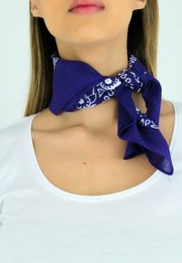 Écharpe violette nouée autour du cou, ornée d'un motif floral et de paisley blanc, composée d'un tissu léger. Portée avec un haut blanc.